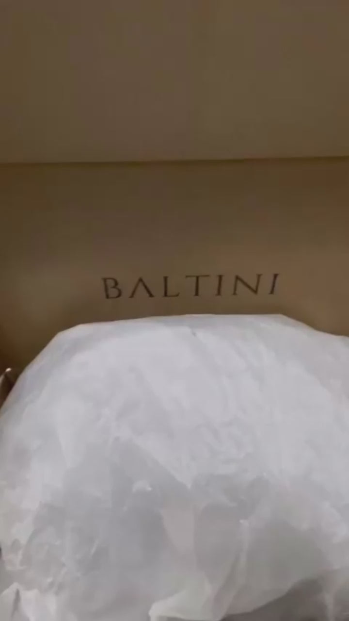 An unboxing video showcasing a luxurious black Givenchy handbag from BALTINI, placed on a soft, white fur surface. The structured leather bag features silver hardware, a detachable long strap coiled neatly beside it, and a BALTINI tag attached. The Givenchy logo is embossed on the front, highlighting its premium design and craftsmanship.